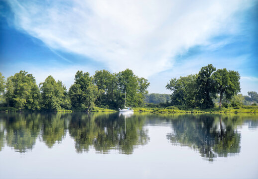 A calm scene looking across a calm body of water to a forested island, reflections, large clouds, nobody