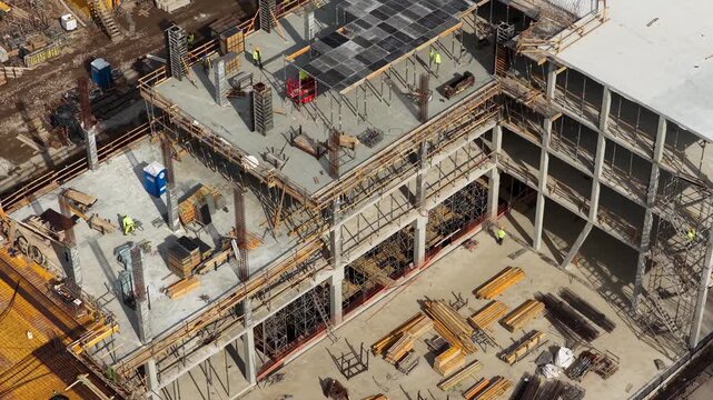 Drone footage capturing a partially completed multi story concrete building with scaffolding, formwork, and materials, highlighting structural progress and active construction environment.