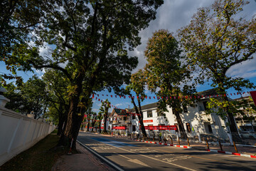 Obraz premium Vientiane Laos: 22 November 2025. A view of a sunlit urban intersection featuring light traffic in front of a prominent government building adorned with flags. The scene captures a calm city