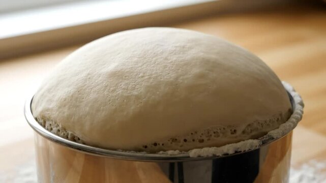 Rising dough in a metal bowl, showing yeast activity, for making fresh homemade bread on a wooden surface