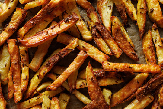 Homemade potato French fries baked in the oven with aromatic spices, close-up view. French fries background