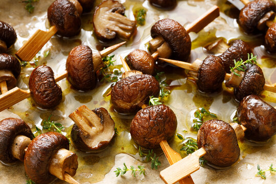 Brown mushrooms skewers seasoned with thyme and olive oil, close up. A delicious vegetarian snack.