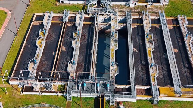 Top down view of rectangular primary sedimentation tanks at plant. Symmetrical aerial shot of parallel water treatment basins with metal walkways and mechanical equipment.