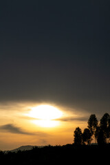Obraz premium Sunset over mountain horizon with tree silhouettes and glowing sky