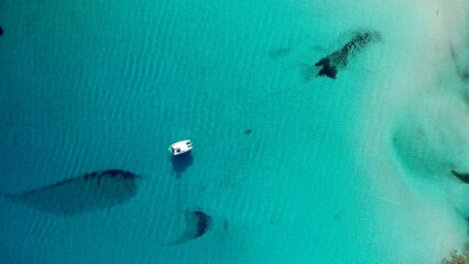 Aerial top-down abstract view of crystal clear turquoise water with underwater rock formations and anchored boat, La Pelosa, Sardinia, Italy © GypsyDjango