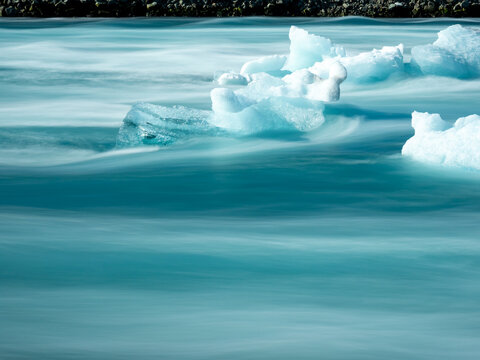 Chunks of ice floating in bright blue water of Iceland's Glacier Lagoon, long exposure