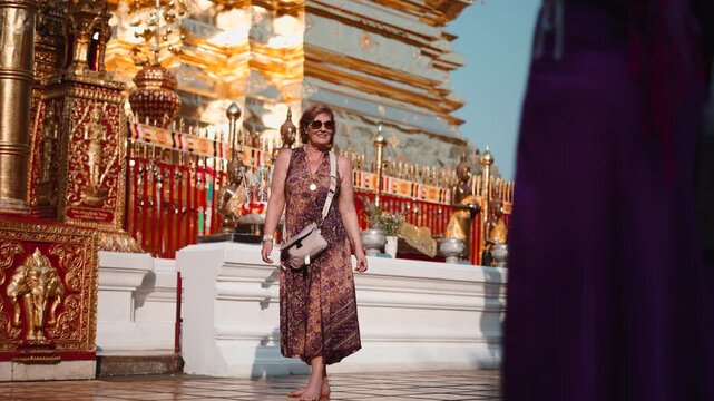 Senior woman smiling and exploring a golden buddhist temple in chiang mai, thailand