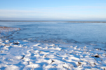 Naklejka premium Landscape, blue sky and ocean with snow in nature for climate change, winter season and morning frost. Space, sea and coastline with ice formation, frozen field and icy conditions from global warning
