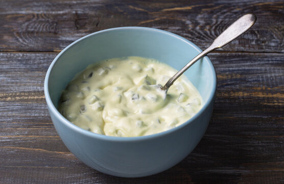 Homemade tartar sauce with pickles in light blue bowl on wooden background, creamy condiment with spoon