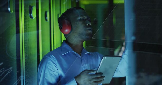 Vertical video: Reading tablet, tech inspecting rack panel in server aisle to verify, red earmuffs