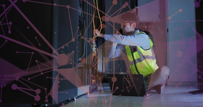 Kneeling Korean tech in hi-vis vest adjusting cables at server rack, taking call while using laptop