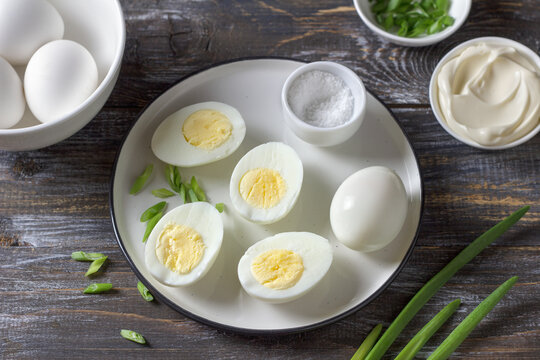 Boiled eggs with green onion, salt and mayonnaise on plate over wooden table