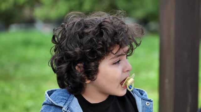 Armenian boy with curly hair and pacifier enjoying childhood outdoors