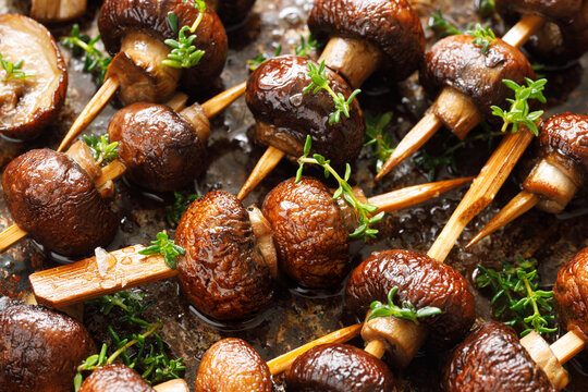 Small grilled skewers of brown mushrooms seasoned with thyme and olive oil, close up. A delicious vegetarian snack.