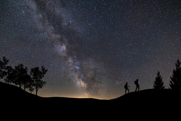 Fototapeta premium Lone person standing on top of rock, pointing with hand towards the Milky Way and the vast expanse of universe. Stunning silhouette of man gazing out into the cosmos. Power of dreams and aspirations.