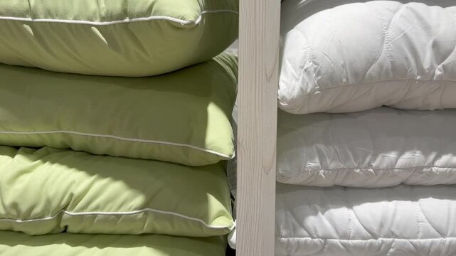 Rows of new green and white soft pillows stacked neatly on wooden shelves in a retail store, with sunlight and shadows moving across them, suggesting the passage of time