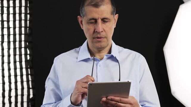 Tablet, filming and man on set with lights reading for documentary interview or podcast episode. Digital technology, research and male journalist recording for online live streaming show with script.