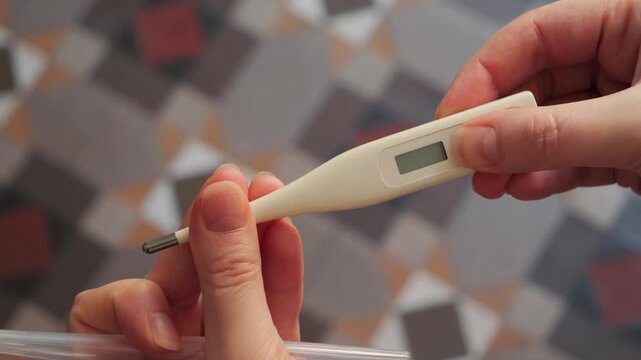 Hand taking a digital thermometer out of a plastic case and pressing the button to turn it on. Close-up of activating a medical device for temperature measurement. High quality 4k footage