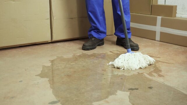 Male worker cleaning-up a slip hazard on the floor of an industrial plant with white mop.