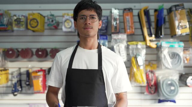 Young male employee working in a hardware store, checking inventory and looking at the camera