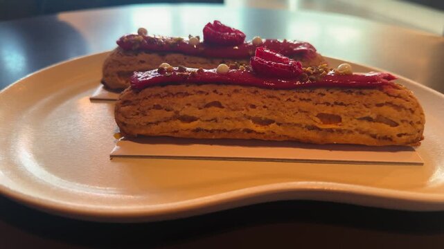 Fresh and delicious eclairs with sweet and sour raspberry cream, served on a white plate in a cozy French cafe. High quality 4k footage