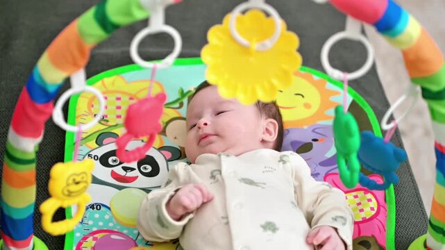 Baby lying under colorful toys on a play mat, reaching out and exploring sensory objects, early development activity, curious and engaged infant in a calm home setting. High quality 4k footage