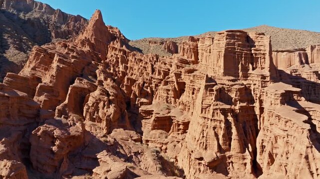 Vast rock formations rise majestically in arid landscape of Kyrgyzstan. Wide drone shot with truck to the right camera movement.