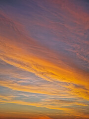 Fototapeta premium Vibrant sunset sky with multicolor layers of textured clouds. The horizon glows in fiery orange and yellow light, while the upper atmosphere transitions into soft, sweeping lavender and indigo tones