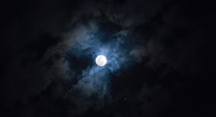 Fototapeta premium Mesmerizing full moonlight shining through night clouds in a celestial sky