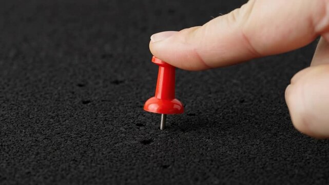 Red Pushpin Being Pushed into Black Cork Board Close Up.