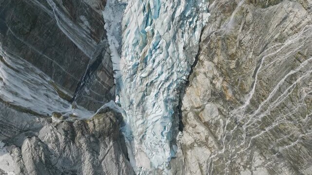 Cinematic top down aerial view of glacier ice and rocky mountains. Abstract geometric pattern of arctic glacier textures and stone cliffs from above. Stunning wild nature drone footage.