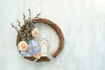 Naklejka premium Easter holiday background. Beautiful easter wreath with angel figurine, egg and rose flowers on light table close up. symbol of Easter, Christianity religion, faith in God, prayer. flat lay.