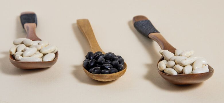Frijol negro y alubia blanca sobre cucharas de madera sobre fondo blanco