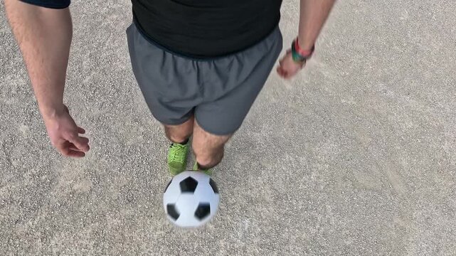First person perspective of a young man performing freestyle soccer tricks. The skilled player is juggling the ball with his feet on an asphalt court
