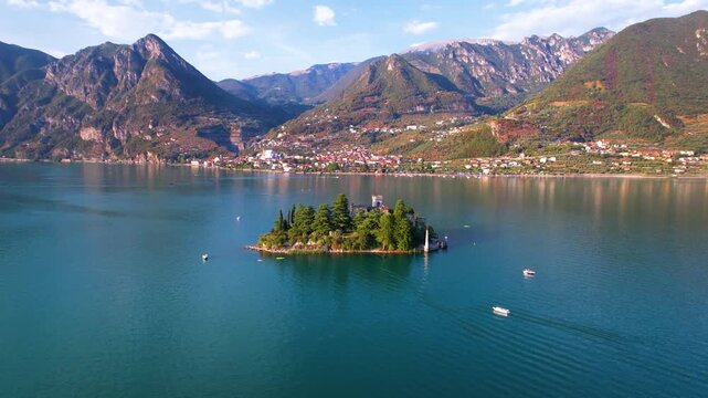 Italy Lake Iseo Loreto Island aerial drone fly-in to medieval castle with canoes on water. Epic Alps mountains and scenic island landscape. Outdoor travel adventure activity Lombardy scenery 4k
