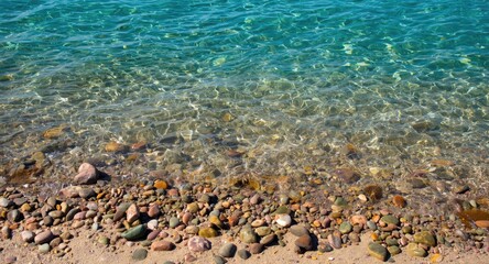 Obraz premium Glossy vibrant round stones scattered across sandy shore adjacent to tranquil turquoise sea reflecting calm