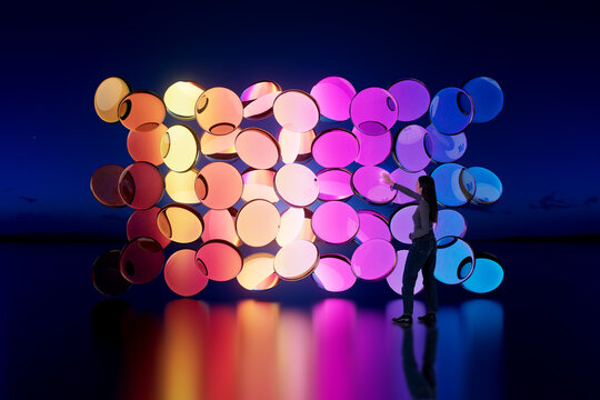 Asian woman touching glowing 3D circular light modules installation in dark environment