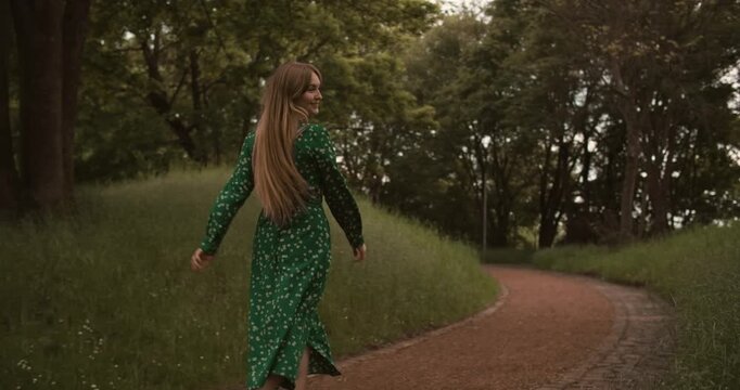 Young beautiful woman walking in long green dress at summer nature. Caucasian European happy girl run with smile in park. Amazing natural women beauty, long blond straight hair. Ukrainian people 4k