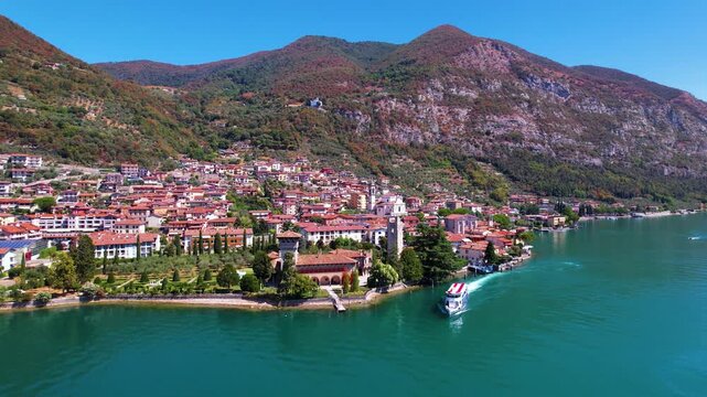 Italy Lake Iseo Aerial 4K Video Drone View of Predore Village and Castle with Tour Boat Departing from Pier Following Boat with Scenic Mountain Landscape Bergamo