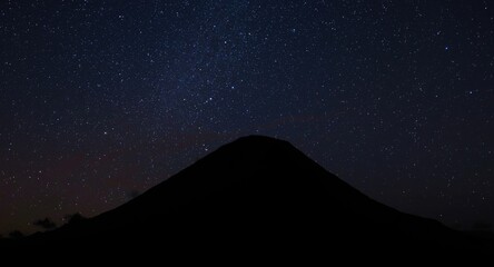 Fototapeta premium Dark silhouette of a volcano erupting under a sparkling night sky