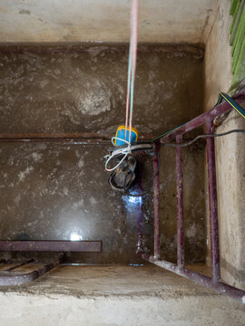 Electric submersible water pump with blue float switch lowered by rope into flooded concrete pit or cellar near metal ladder for drainage and flood relief.