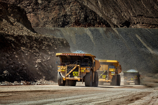 ultra-class haul trucks thunders through the terraced walls of a vast open-pit copper mine, each massive vessel loaded with freshly blasted ore and moving with the precision of a well-orchestrated 