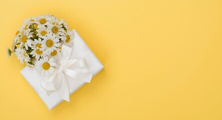 Fototapeta premium Birthday and Mother's Day concept featuring overhead view of white ribbon gift and chamomile bouquet on yellow background