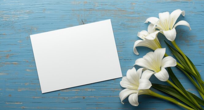 Greeting card mockup with white blank card adjacent to white Alstroemeria blooms on a blue painted wooden table