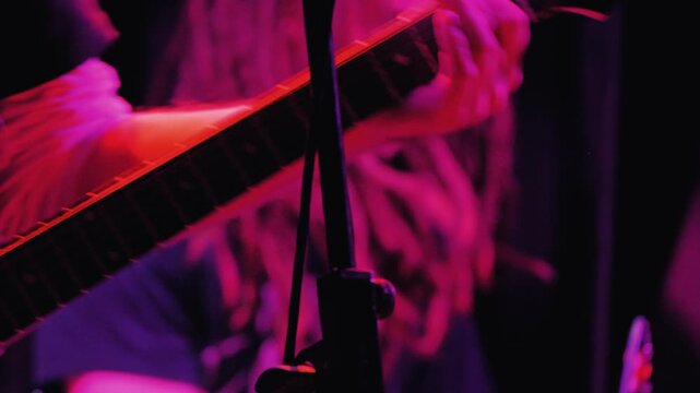 A close-up, dynamic shot of a guitarist's hands playing the fretboard of an electric guitar during a live performance. A drummer is in background. The energetic and tense atmosphere of a club concert