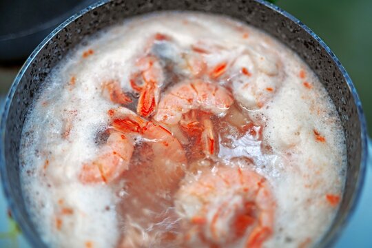 Large peeled red langoustines boiling in water with abundant protein foam in a pot. Seafood cooking process.