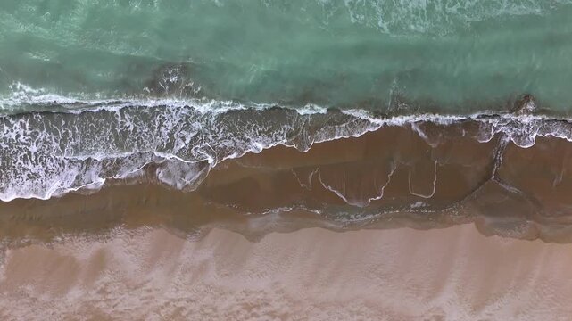 Drone top view of the Caspian Sea shoreline where turquoise waves meet a sandy beach forming clean symmetrical patterns empty coastal scene with clear water and natural textures