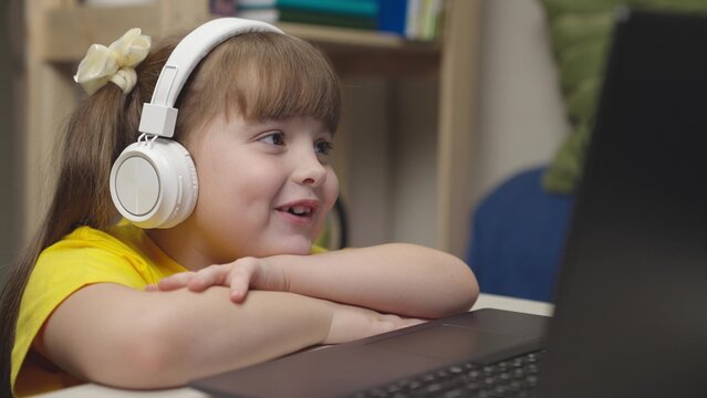 little schoolgirl headphones does homework while sitting digital laptop. distance learning online students. children funny communication through internet video communication. lessons monitor display