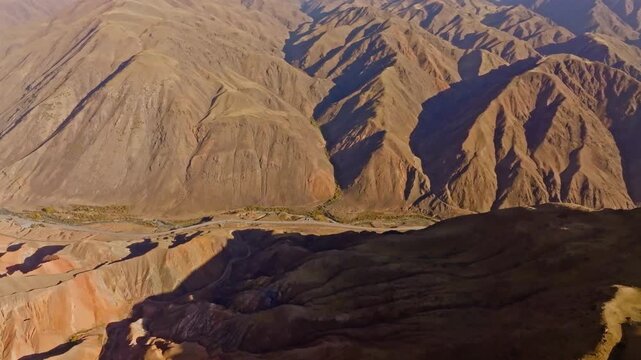 Aerial view captures dramatic eroded sandstone mountains in Kyrgyzstan's Konorchek canyons. Vast landscape features winding road through serene valley.