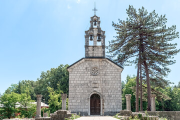 Fototapeta premium Symmetric view of the Court Church on Cipur in Cetinje, Montenegro. Stone Orthodox chapel with a prominent belfry surrounded by ancient ruins and pine trees in Europe